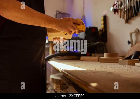Man working in assembly shop using sanding block to remove imperfections on wood piece. Carpenter using coarse grade sandpaper to do manual sanding, employed in furniture assembly workspace Stock Photo