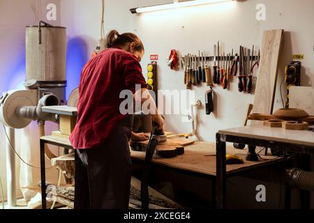 Artisan in studio using orbital sander with fine sandpaper on lumber to achieve smooth finish. Creative woodworker in carpentry shop uses angle grinder to create wood art Stock Photo