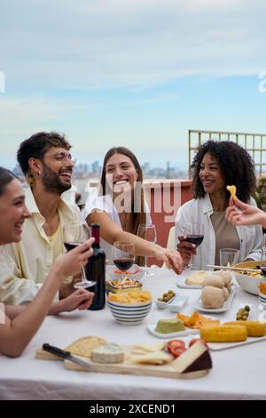 Laughing group of diverse young friends enjoying lunch together outdoors celebrating party rooftop.  Stock Photo