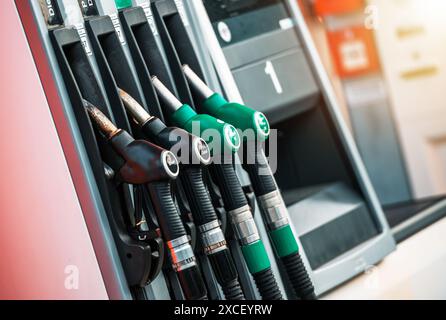 A close-up shot of several fuel pumps at a gas station. The pumps are black and silver, with green handles. The pumps are mounted on a silver metal pa Stock Photo