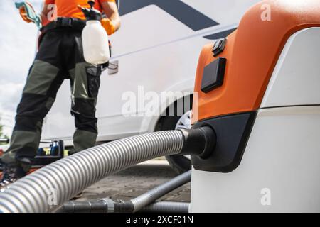 A worker cleans a white motorhome using a large industrial vacuum cleaner. The hose is connected to the vacuum and is on the ground next to the motorh Stock Photo