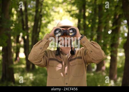 Forester with binoculars examining plants in forest Stock Photo
