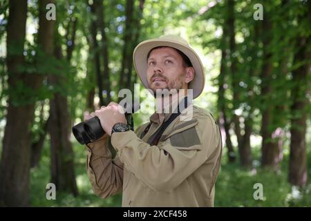 Forester with binoculars examining plants in forest Stock Photo
