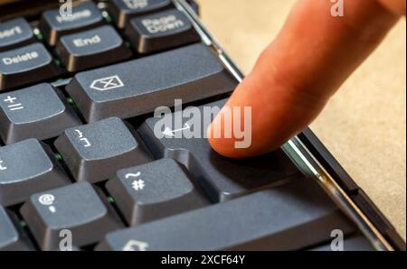Man pressing an enter key on a laptop computer keyboard, finger pushing the key object detail closeup, one person. Accepting, confirming an action, se Stock Photo