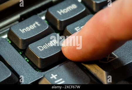Finger pressing the Delete key on a simple laptop computer keyboard, object macro detail, extreme closeup. Deleting files, removing content, digital d Stock Photo