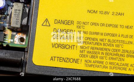 A yellow danger label with heat exposure caution message in various languages and a exclamation mark triangle on a generic electronic device laptop ba Stock Photo
