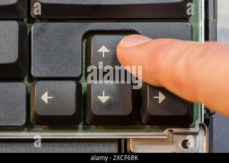 Man pressing the up arrow key on a simple laptop computer keyboard, top down table top view from above. Finger presses the forward arrow, moving forwa Stock Photo