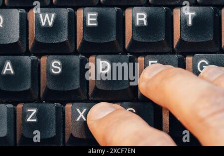 Mans hand resting on an old retro style aesthetic laptop computer keyboard with thick keys, top view shot from above, one person. Retro computing, typ Stock Photo