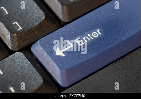 Blue enter key on a modern laptop computer keyboard object symbol macro detail, extreme closeup, nobody. Highlighted enter key concept, no people. Con Stock Photo