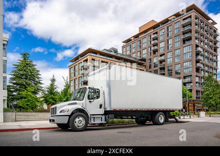 Industrial carrier middle duty day cab rig semi truck with box trailer for local freights standing with open back door on the urban city street making Stock Photo