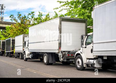 Industrial carrier middle duty rig semi trucks with day cab and refrigerated box trailers for local freights standing in line on the urban city street Stock Photo