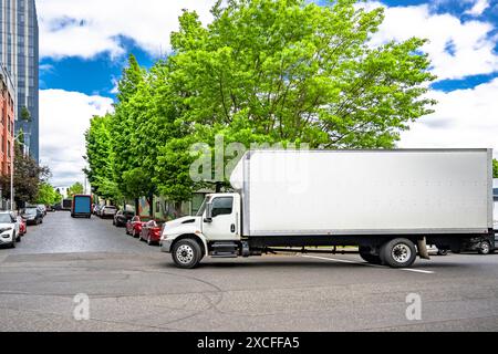 Industrial carrier middle duty day cab rig semi truck with long box trailer for local freights transporting commercial cargo in turning on the city st Stock Photo