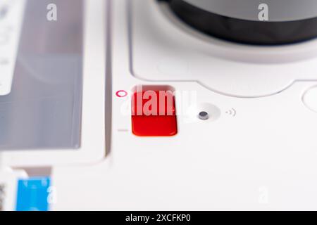 A white robot with a red button on the bottom. Red button to turn on or off the robot vacuum cleaner. Robot vacuum cleaner on a white background. Stock Photo