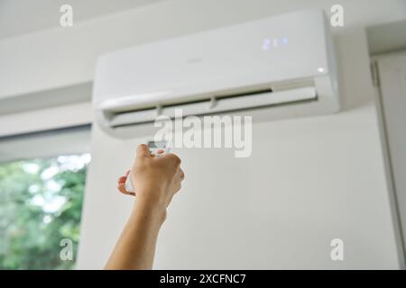 Adjusting air conditioner temperature with remote control. Hand holds remote control and setting comfortable temperature on climate system in apartmen Stock Photo