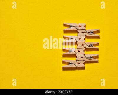 Wooden clothespins in a row on yellow background. Creative minimalistic design, flat layout, copy space. Stock Photo