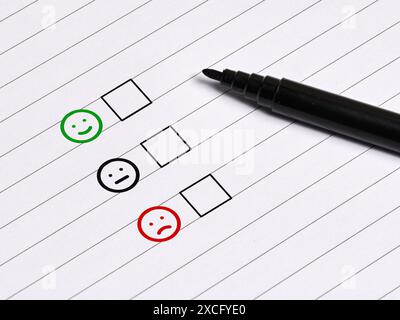 Customer satisfaction survey concept. Happy, neutral and sad emoticon faces with checkboxes on a notebook with pen. Stock Photo