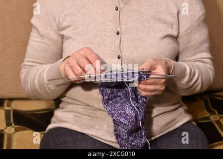 Close-up of female hands knitting a woolen sock with knitting needles. Stock Photo