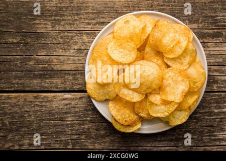 Crispy Potato Chips on plate on a wooden table. Top view. Stock Photo