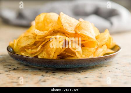 Crispy Potato Chips on plate on a kitchen table. Stock Photo