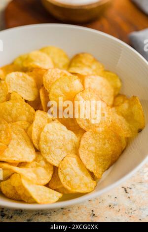 Crispy Potato Chips in bowl on a kitchen table. Stock Photo