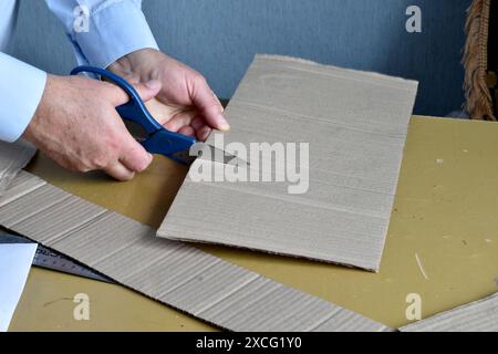The picture shows the hand of a man who cuts a sheet of cardboard with scissors. Stock Photo