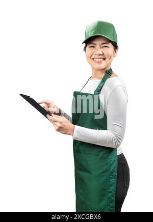 Asian seller wear green apron and green cap smiling with hand holding digital tablet isolated on white Stock Photo
