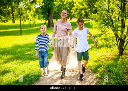 Happy mother is walking with her sons in park. They are holding hands and enjoying summer day. Stock Photo