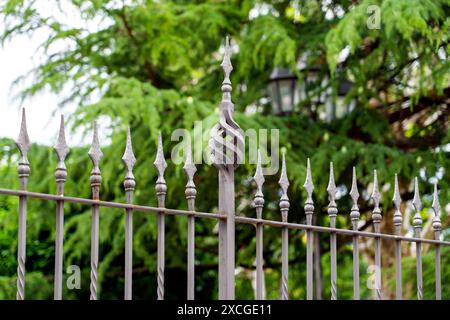 Decorative iron fence top, featuring intricate metalwork and a unique spiral design. The backdrop is a blur of green foliage, suggesting a serene outd Stock Photo