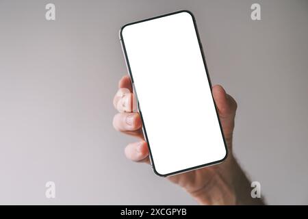Tilted vertically held smartphone with blank white mockup screen in male hand, selective focus Stock Photo