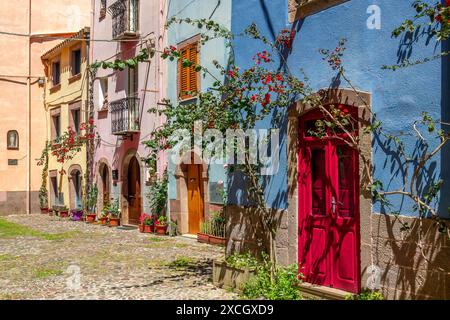 Colorful houses with flowers pots and bouguinvillea in a picturesque cobbled street in the old medieval village of Bosa, Sardinia island, Italy Stock Photo