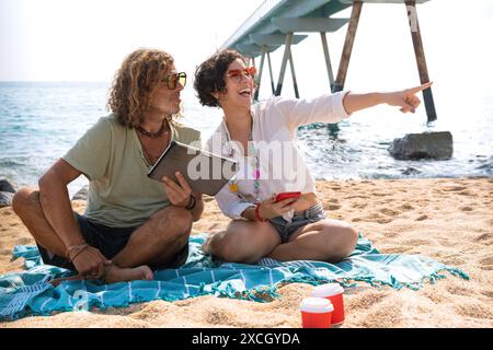 Couple on the beach,pointing to the location of the hotel with the tablet Stock Photo