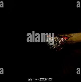 Macro shot of a lit rolled cigarette isolated on the black background with little flame. Stock Photo