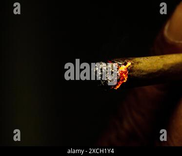 Macro shot of a lit rolled cigarette isolated on the black background with little flame. Stock Photo