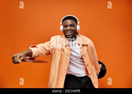 Stylish black man wearing headphones holding record on orange background. Stock Photo