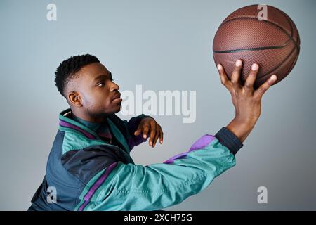 A fashionable young African American man in stylish attire holds a basketball. Stock Photo