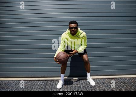 A trendy young man in a green hoodie holds a basketball. Stock Photo