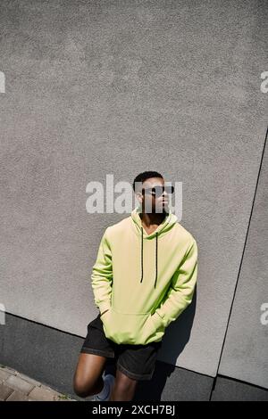 Handsome African American man in a yellow hoodie leans against a wall. Stock Photo