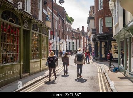 People walk past shops and stores in High Petergate in the historic city of York, North Yorkshire, England. The city is a popular tourist destination. Stock Photo