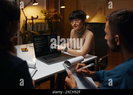 Developer showing programming code on laptop screen and discussing with team Stock Photo