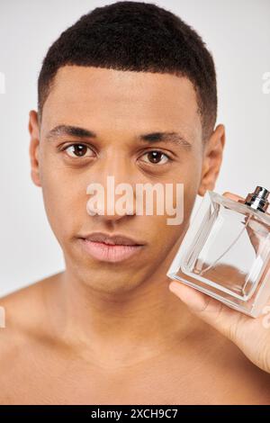 Young man confidently holds a bottle of perfume. Stock Photo