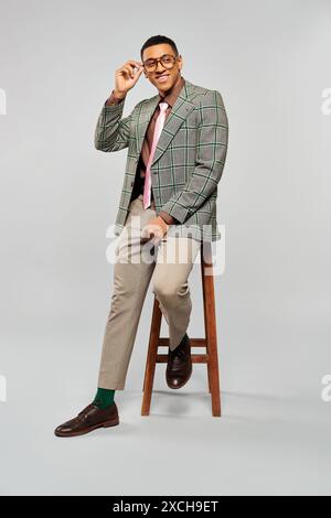 Man in plaid blazer and tie sitting on stool. Stock Photo