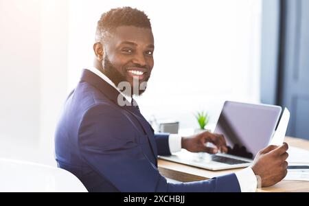Cheerful black general manager checking reports, sitting in office Stock Photo