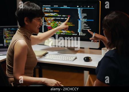 Female developers discussing programming code on computer screen Stock Photo