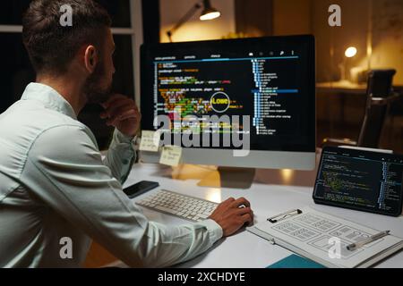 Pensive developer looking at programming code on computer screen Stock Photo