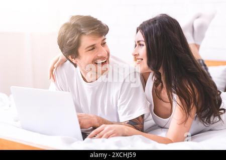 Happy Couple Laughing While Using Laptop in Bed Stock Photo