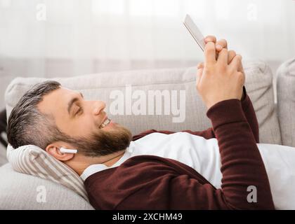 Man Smiling While Lying on Couch and Using Smartphone Stock Photo