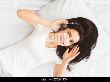 Young Lady Enjoying Music With Headphones While Lying on Bed Stock Photo