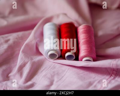Multicolored sewing threads on paper bobbins and spools on pink fabric. Threads for needlework, hobbies and recreation. Necessary item for every famil Stock Photo
