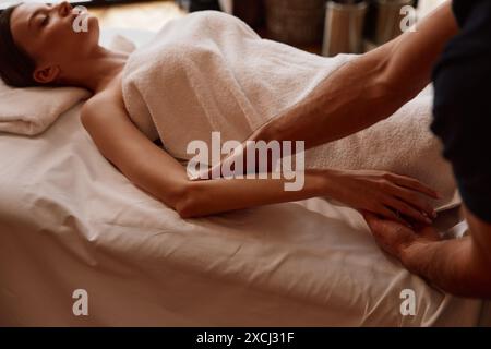 Masseur massaging arms of relaxing woman client lying on couch Stock Photo