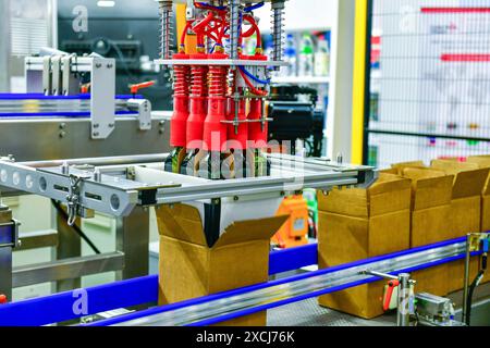 A robot arm is loading glass bottles into boxes on an automated industrial machine on a production line. Stock Photo